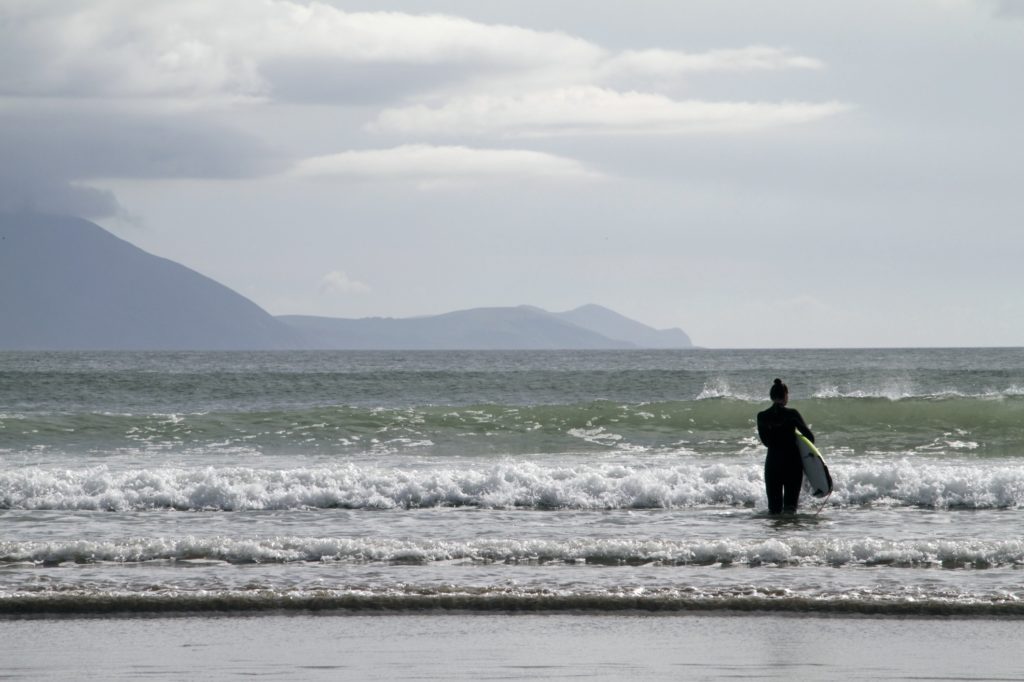 woman-with-a-surfing-board-in-the-sea-surrounded-by-the-hills-under-a-cloudy-sky-in-ireland-171718954